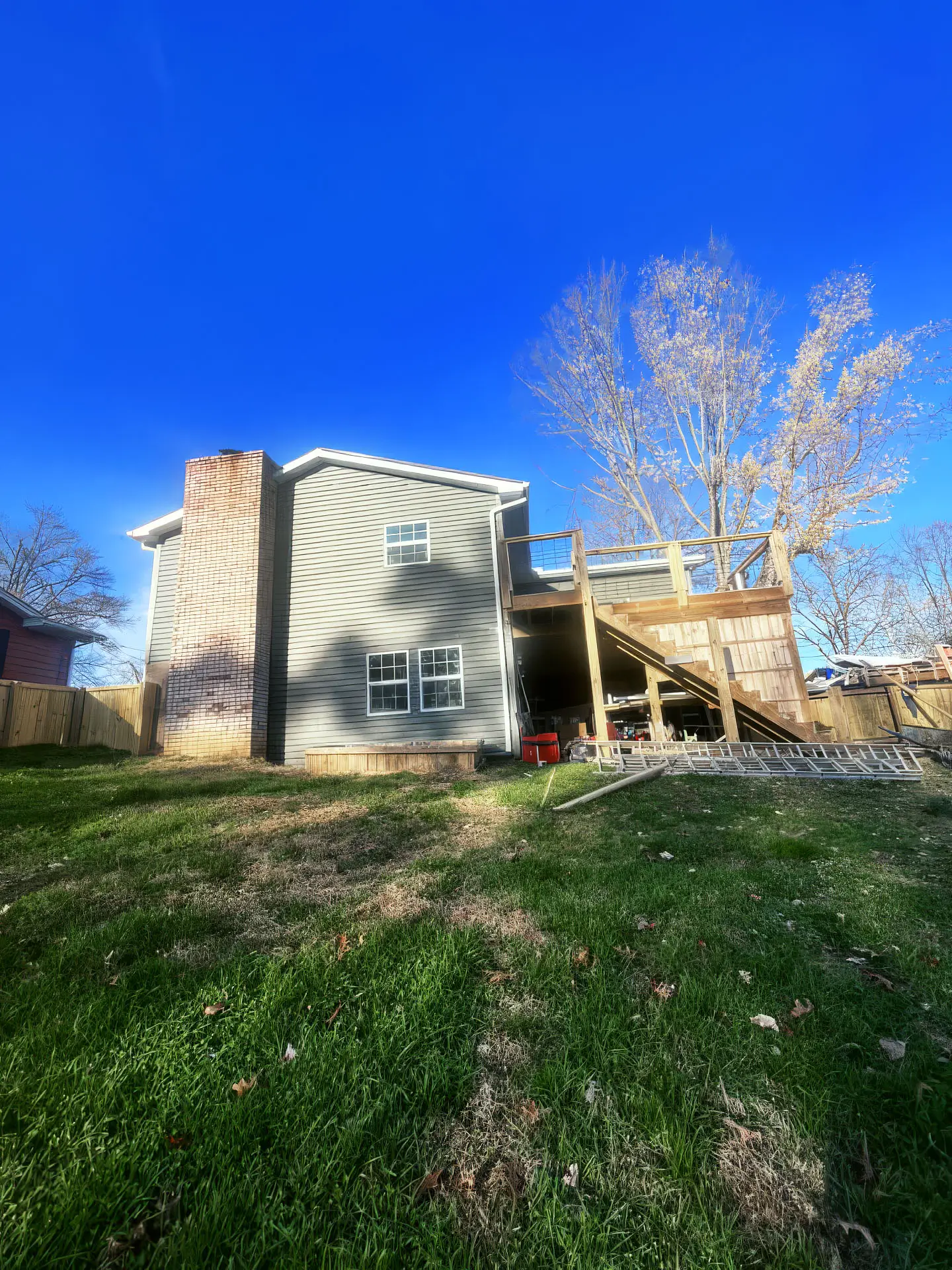 A house featuring a deck and a ladder leaning against it, set in a sunny outdoor environment.